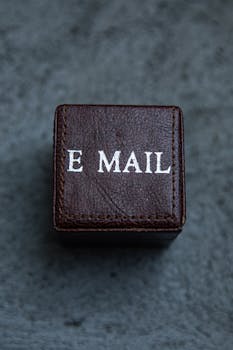 Brown leather square box with 'E MAIL' text on a gray surface, modern still life